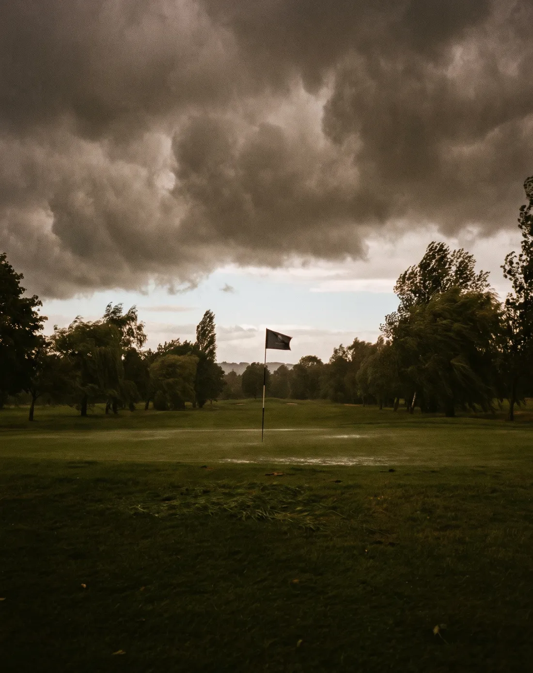 Dunkle Gewitterwolken über einem Fairway, die Fahne flattert im Wind